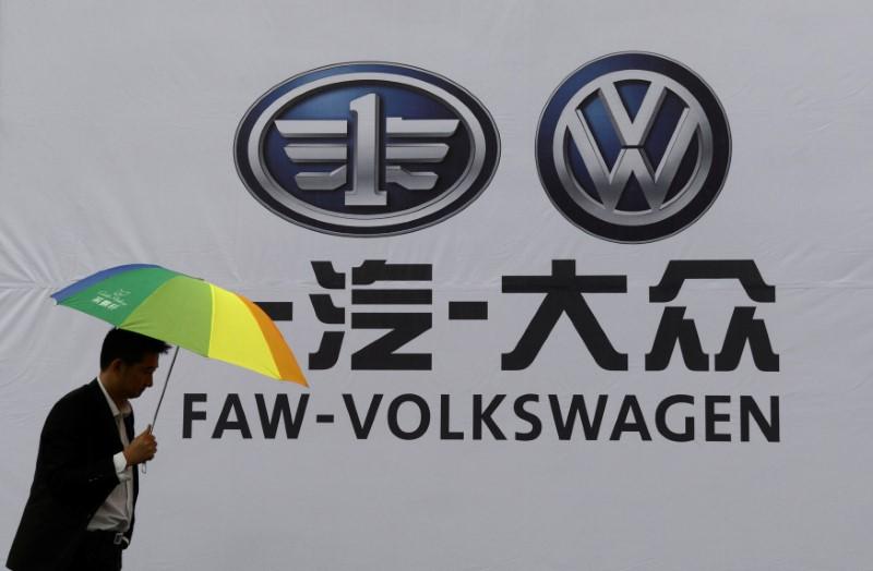 FILE PHOTO: A man holds an umbrella as he walks past a company logo of FAW-Volkswagen at an automobile exhibition in Fuyang